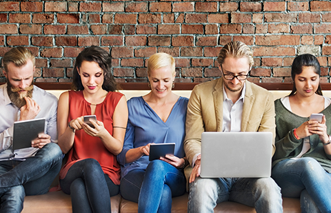 Eine Gruppe von vier Personen auf einem Sofa am Handy und am Laptop